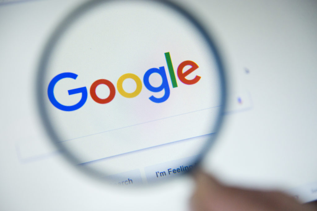 Google homepage on the screen under a magnifying glass. SEO maintenance is needed to maintain Google rankings. 